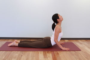 7.息を吸いながら、腰を床に降ろし、手の平しっかり開いて床を押しながら上体を起こして後ろへ反らせる。両脚は揃えたままにし、肩は下げて肩甲骨を引き寄せるように後ろへ引いて胸をひらく。上後方を見上げる。